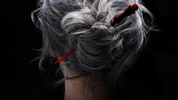 Das graue Haar einer Frau ist mit roten Haarnadeln geschmückt.