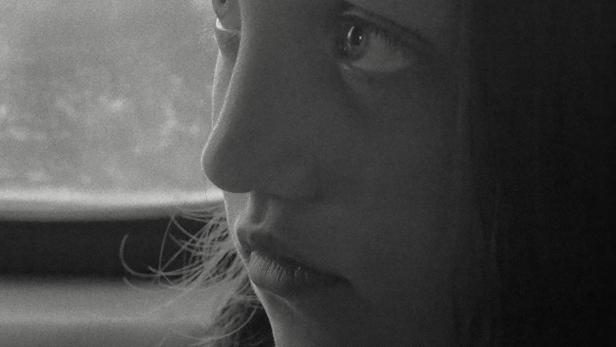 Ein Schwarzweißporträt eines jungen Mädchens, das aus dem Fenster schaut.