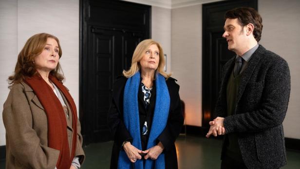 Drei Personen stehen in einem Flur und unterhalten sich.