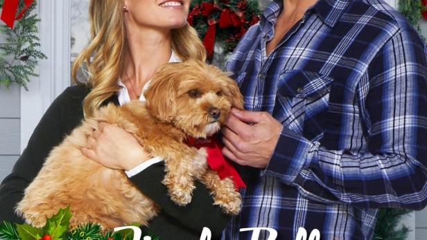 Ein Mann und eine Frau halten einen kleinen Hund vor einem weihnachtlich geschmückten Haus.