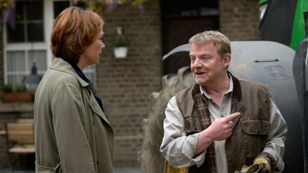 Ein Mann und eine Frau unterhalten sich vor einem Traktor.