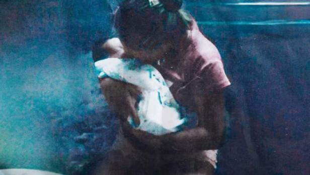 Eine Mutter hält ihr Baby im Arm, im Hintergrund der Titel „Maloqueridas“.