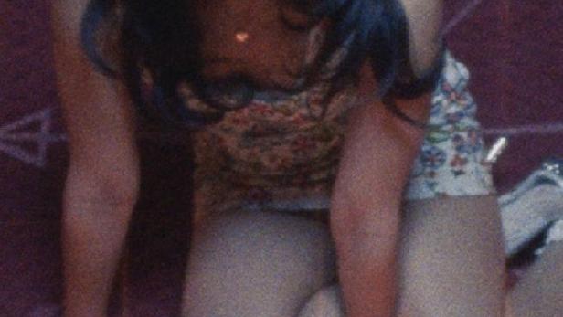 Eine Frau kniet auf einem roten Teppich mit einem aufgemalten Pentagramm.