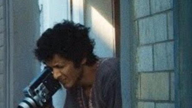 Ein Mann filmt mit einer alten Super-8-Kamera aus einem Fenster.