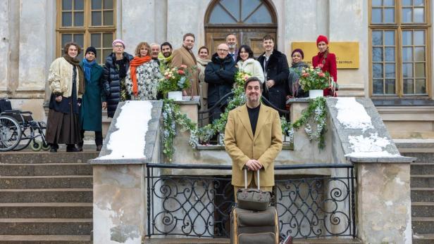 Ein Mann mit Gepäck steht vor einer Gruppe von Menschen auf einer Treppe.