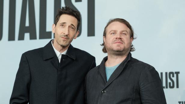 Adrien Brody und Brady Corbet posieren zusammen vor einer Wand mit dem Schriftzug „The Brutalist“.