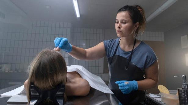 Eine Bestatterin untersucht eine Leiche auf einem Tisch.