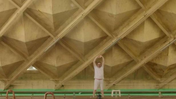 Eine Gruppe von Menschen macht Wassergymnastik in einem Schwimmbad mit markanter Deckenstruktur.