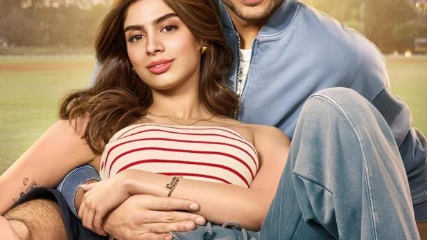 Ein junges Paar sitzt im Freien, der Mann hat seinen Arm um die Frau gelegt.