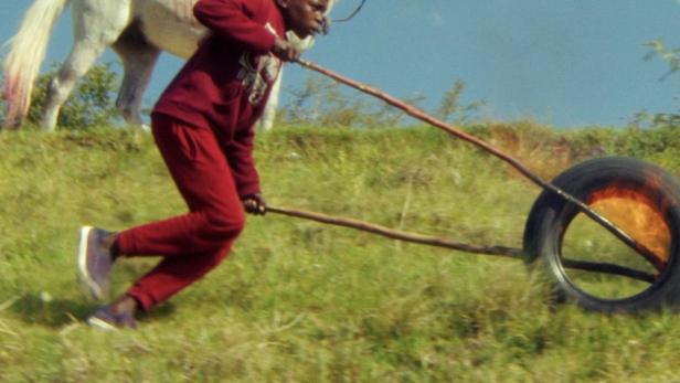 Ein Junge rennt einen Hügel hinunter und zieht einen Reifen, während ein anderer auf einem Pferd reitet.