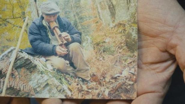 Eine Person hält ein Foto von einem Mann, der in einem Wald sitzt und eine Pfeife raucht.