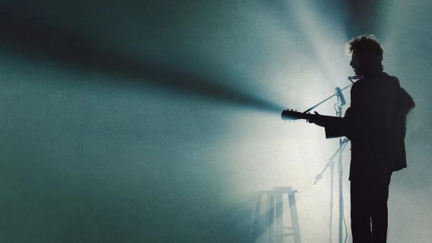 Die Silhouette eines Musikers mit Gitarre und Mundharmonika auf einer Bühne.