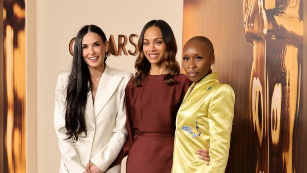 Demi Moore, Zoe Saldana und Cynthia Erivo posieren zusammen vor einem Oscar-Hintergrund.