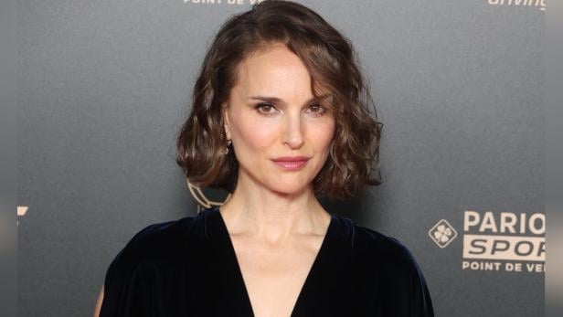 Ein Porträt von Natalie Portman mit gewelltem Haar vor einem dunklen Hintergrund.