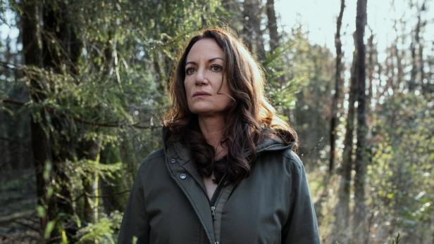 Eine Frau steht nachdenklich in einem Wald.