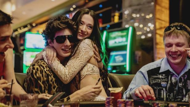 Eine Frau umarmt einen Mann mit Sonnenbrille an einem Spieltisch in einem Kasino.