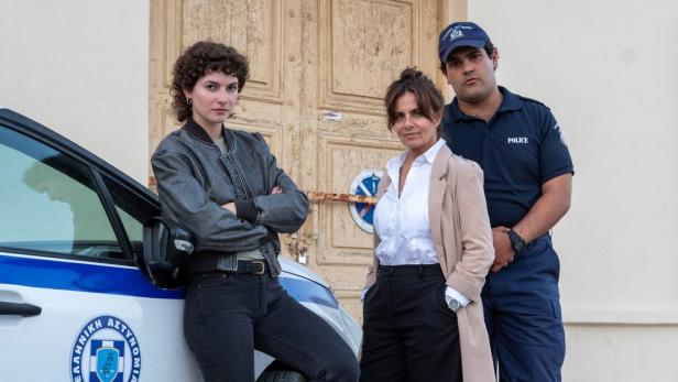 Drei Personen, vermutlich Polizisten, stehen vor einem Polizeiwagen.