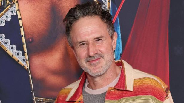 David Arquette posiert vor einem Filmposter.