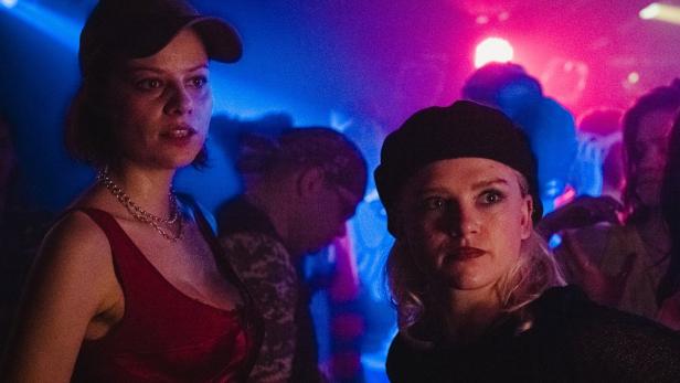 Zwei junge Frauen stehen in einer Menschenmenge mit blauem und pinkem Licht.