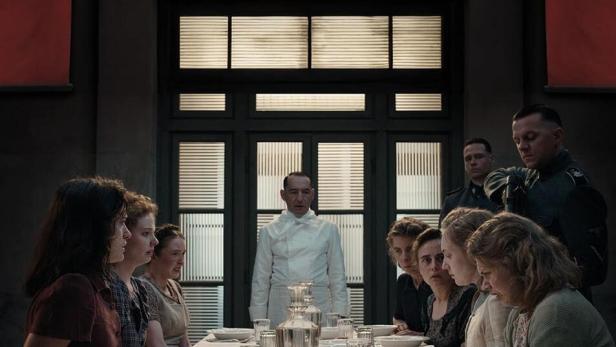 Das Filmplakat für „Le Assaggiatrici“ zeigt Frauen, die an einem Tisch sitzen, und einen Mann in Kochkleidung.