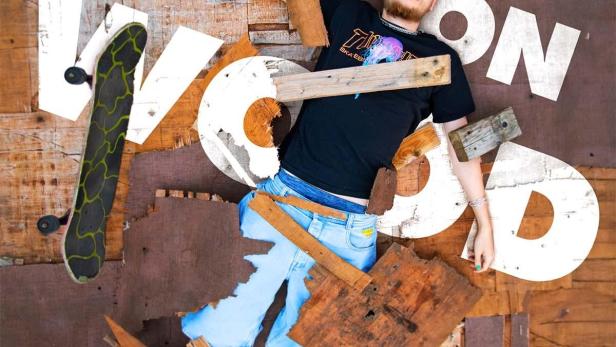 Ein Mann liegt umgeben von Holzstücken und den Buchstaben des Wortes „Knock on Wood“.