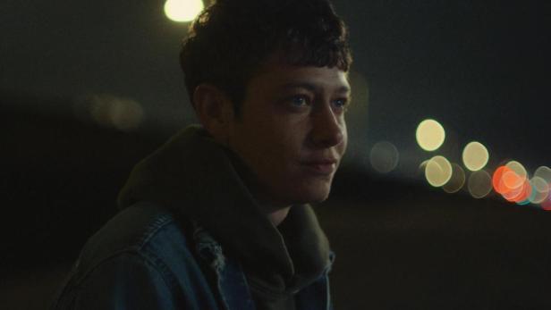 Ein junger Mensch vor dem Hintergrund von Lichtern, möglicherweise ein Filmplakat für „Outerlands“.