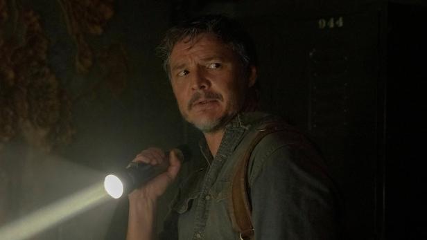 Pedro Pascal als Joel in einer dunklen Szene aus „The Last of Us“ mit einer Taschenlampe.