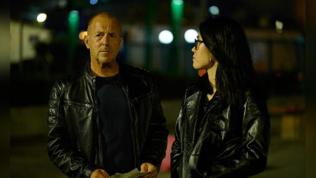 Ein Mann und eine Frau in Lederjacken stehen nachts auf der Straße.