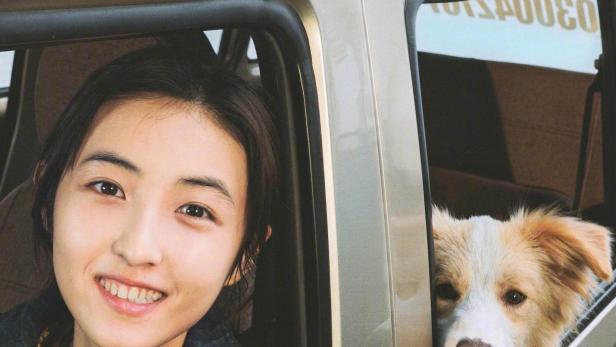 Eine junge Frau und ein Hund schauen aus den Fenstern eines Autos.