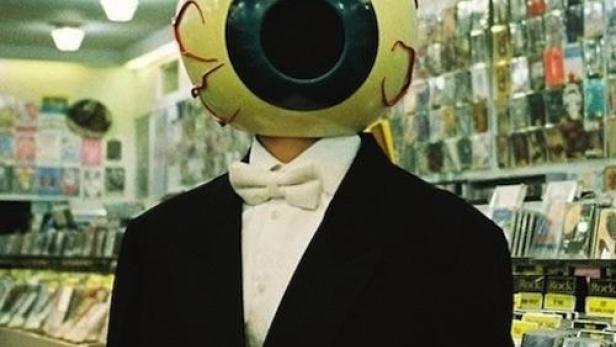 Eine Person mit einem Augapfel-Kopf und Zylinder in einem Geschäft.