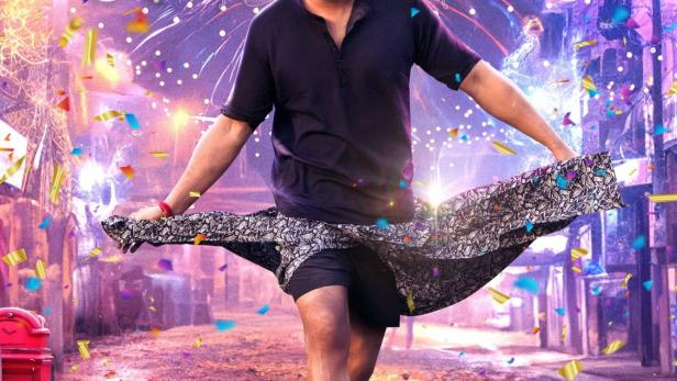 Ein Mann tanzt auf einer Straße vor dem Hintergrund des Filmplakats „Raja Saab“.