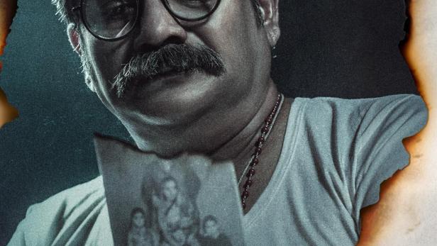 Ein Mann mit Brille betrachtet ein verbranntes Foto einer Familie.