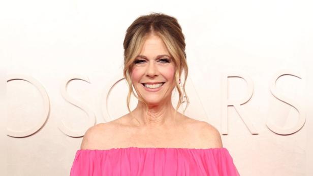 Rita Wilson in einem pinkfarbenen Kleid vor einer Wand mit der Aufschrift „Oscars“.