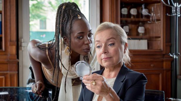 Eine Frau mit Spiegel wird von einer anderen Frau aufmerksam beobachtet.