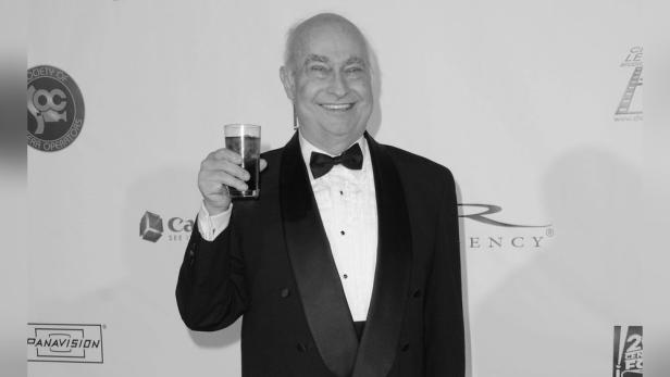 Robert Trebor im Smoking mit einem Getränk in der Hand.