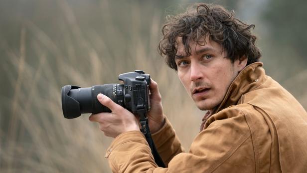 Ein Mann mit lockigem Haar fotografiert mit einer Spiegelreflexkamera.