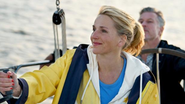 Eine Frau steuert ein Segelboot, ein Mann steht im Hintergrund.