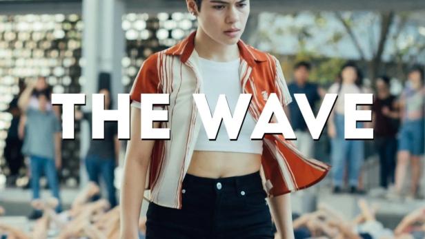 Eine junge Frau steht vor einer Gruppe liegender Menschen; Filmposter für „The Wave“.