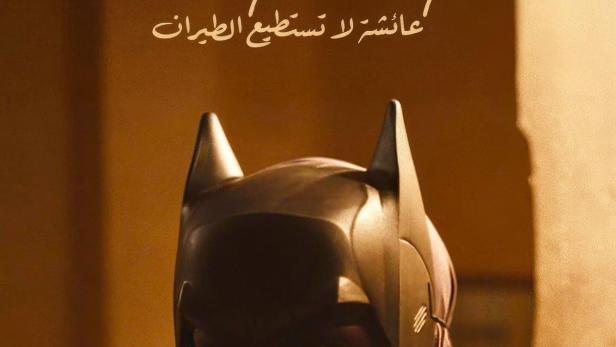 Eine Frau mit Hijab trägt eine Batman-Maske; Filmtitel „Aisha Can't Fly Away“ im Hintergrund.