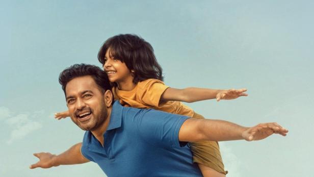 Ein Vater trägt seinen Sohn Huckepack am Strand, beide mit ausgestreckten Armen wie fliegend. Über ihnen der Titel „Sarkeet“.