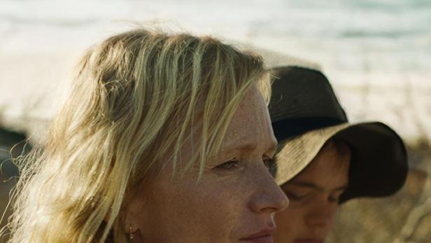 Eine Frau und ein Kind stehen am Strand und schauen in die Ferne.