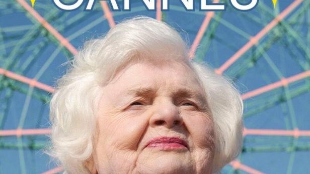 Porträt einer älteren Frau vor einem Riesenrad, mit dem Text „Eleanor is going to Cannes“.