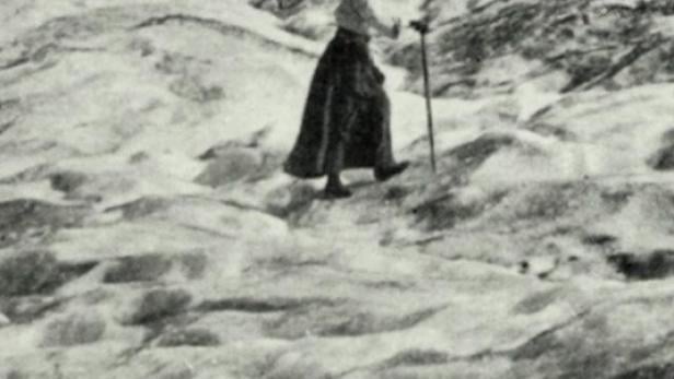 Eine Frau mit Stock wandert in einer Berglandschaft.