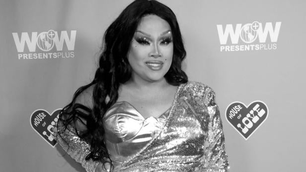 Jiggly Caliente in einem glitzernden Kleid posiert vor einem WOW Presents Plus-Hintergrund.