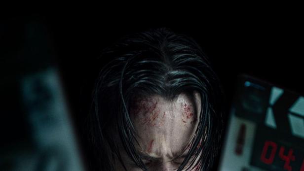 Ein blutverschmierter Keanu Reeves hält eine Filmklappe für „John Wick“ vor dem Gesicht.