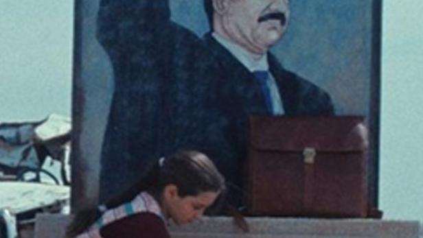 Ein junges Mädchen hockt vor einem Denkmal mit einem Porträt von Saddam Hussein und hält ein Huhn.