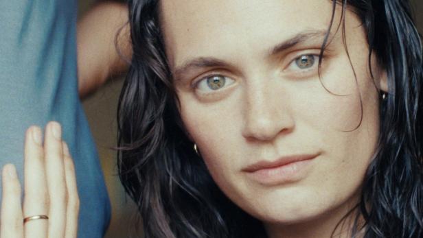 Porträt einer Frau mit dunklen, gewellten Haaren und einem grauen T-Shirt.