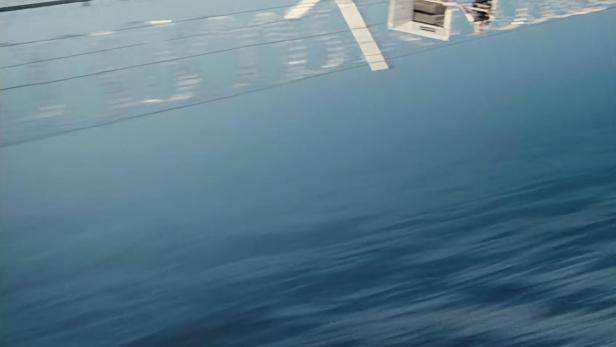 Das Filmplakat für „Moria Six“ zeigt eine Spiegelung eines Gebäudes im Wasser.