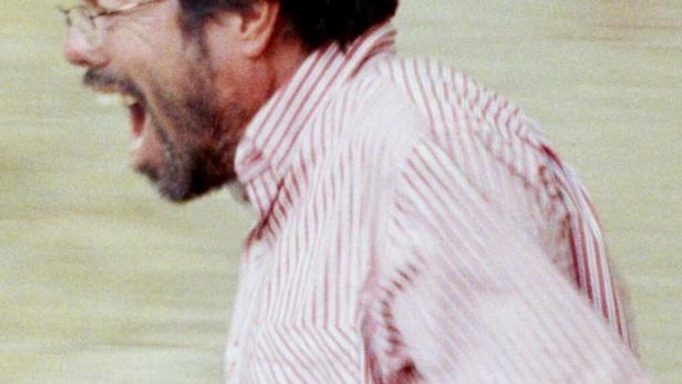 Ein Mann mit Brille und gestreiftem Hemd schreit oder singt.