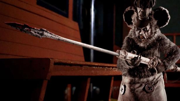 Eine gruselige Ratte in Kochkleidung hält einen blutigen Speer.